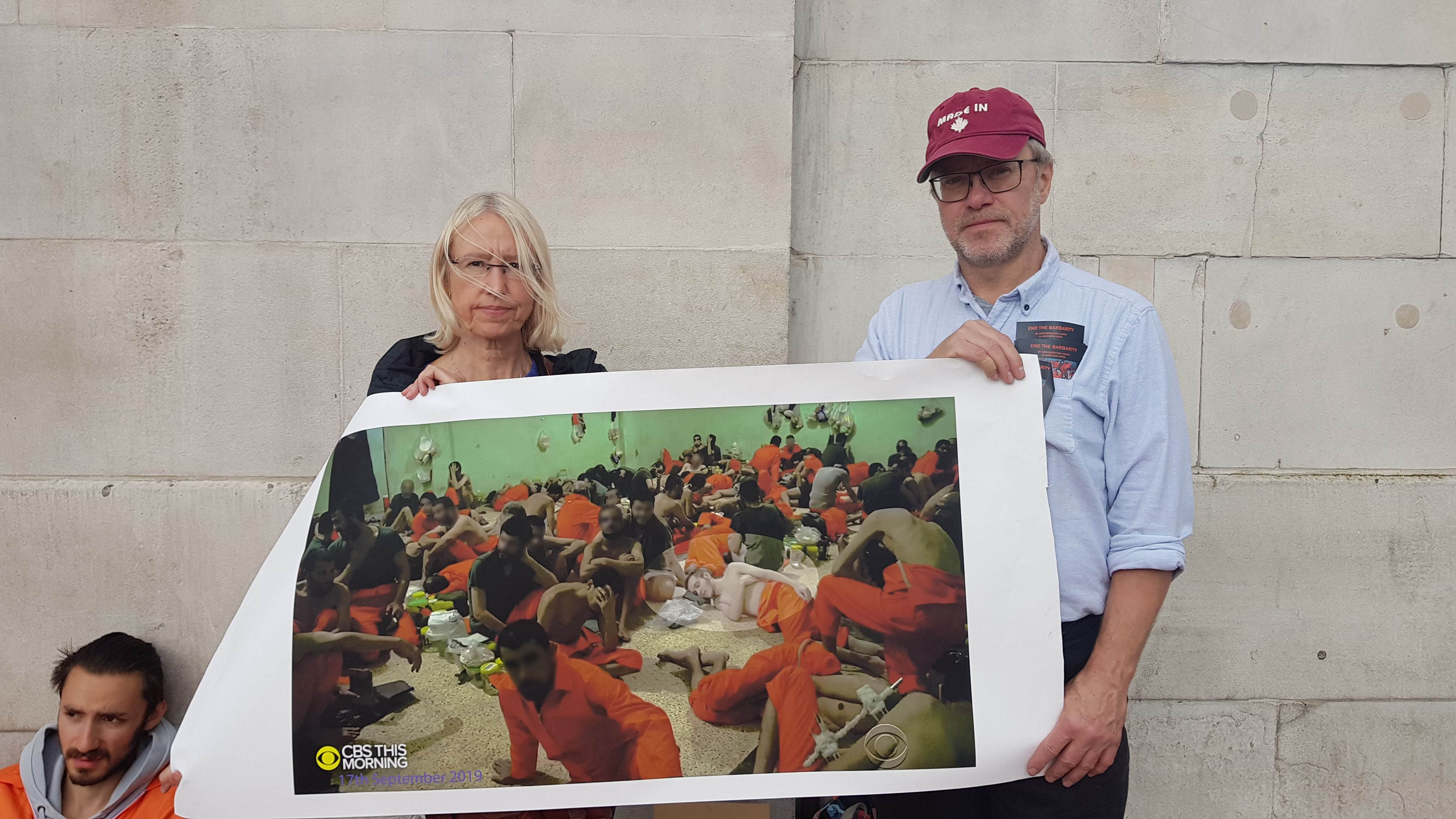 A man and woman hold up a poster of ISIS prisoners