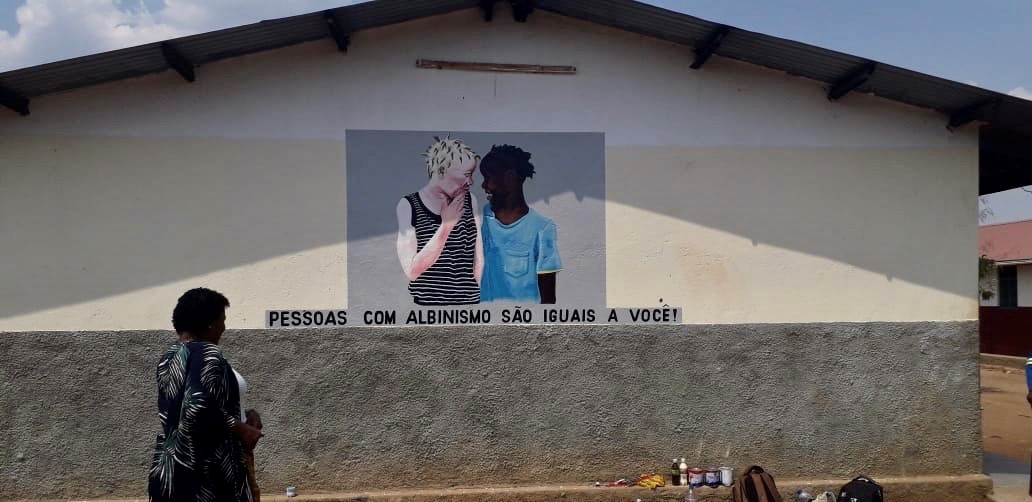 Flavia Pinto, la directrice d'Azemap, une association mozambicaine qui soutient les personnes atteintes d'albinisme, photographiée devant une peinture sur le mur d’une école dans la province de Tete, au Mozambique. Message sous la peinture : « Les albinos sont des personnes comme vous! »