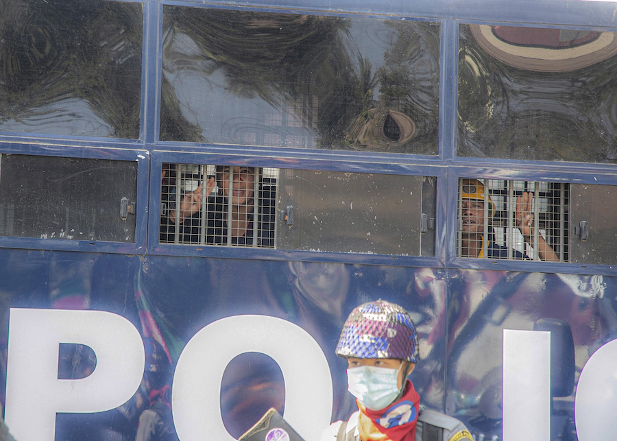 Deux manifestants aperçus derrière les barreaux des petites fenêtres d’un véhicule de police à Mandalay, au Myanmar, le 9 février 2021. Leur salut à trois doigts symbolise leur opposition au coup d’État du 1er février. 