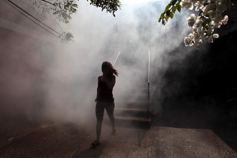 Uma mulher corre de seu apartamento enquanto trabalhadores de saúde fumigam o bairro Altos del Cerro como parte de medidas preventivas contra o vírus Zika e outras doenças transmitidas por mosquitos em Soyapango, El Salvador. 21 de janeiro de 2016.