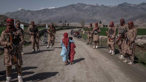 Two children walk by armed soldiers in the countryside