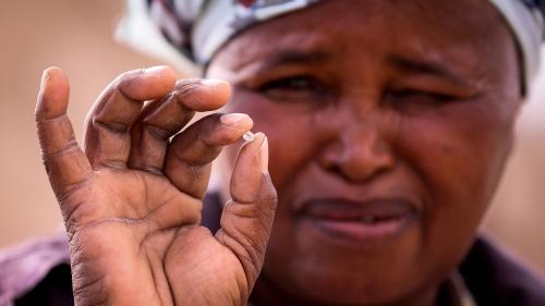 A woman squints while holding a small diamond in her fingers