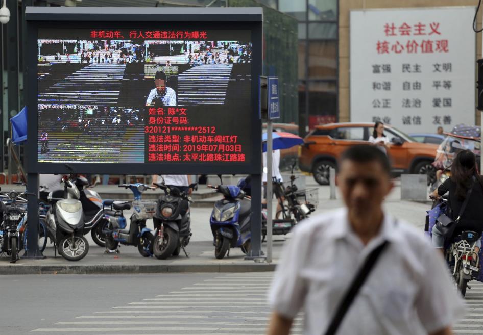 Des piétons traversent un carrefour alors qu'un grand écran électronique assisté par un système de reconnaissance faciale montre l'image d'un piéton en infraction à l'intersection dans la ville de Nanjing, dans la province du Jiangsu (est de la Chine), le 4 juillet 2019.
