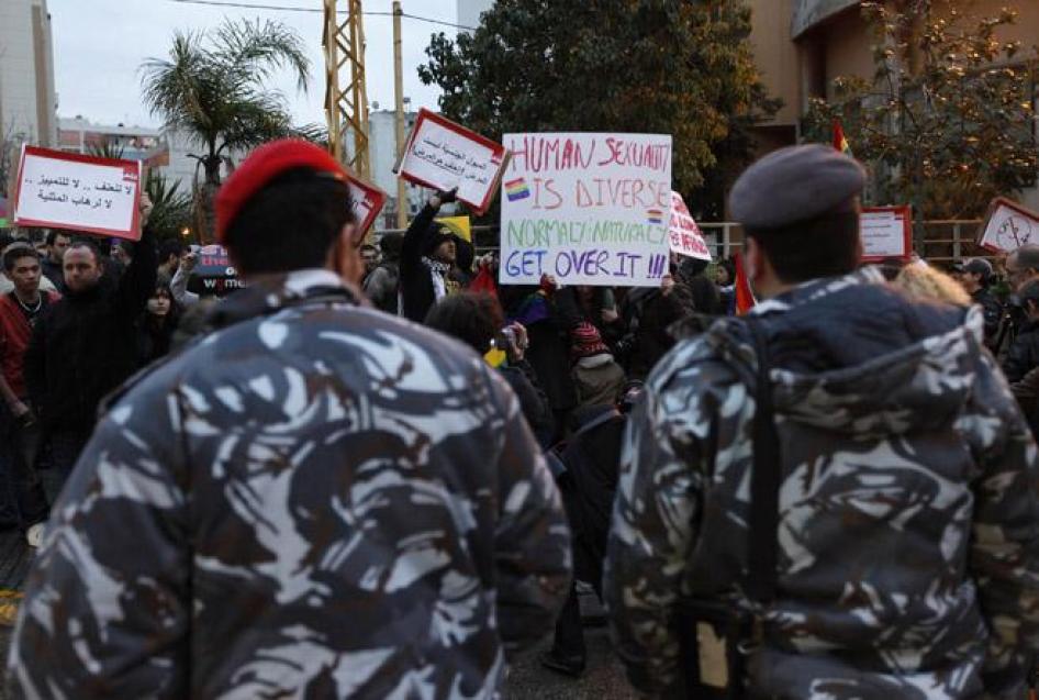 أفراد من الشرطة اللبنانية يقفون في مواجهة معتصمين يحملون لافتات للمطالبة بحقوق المثليين/ات ومزدوجي/ات التوجه الجنسي ومتحولي/ات النوع الاجتماعي. 