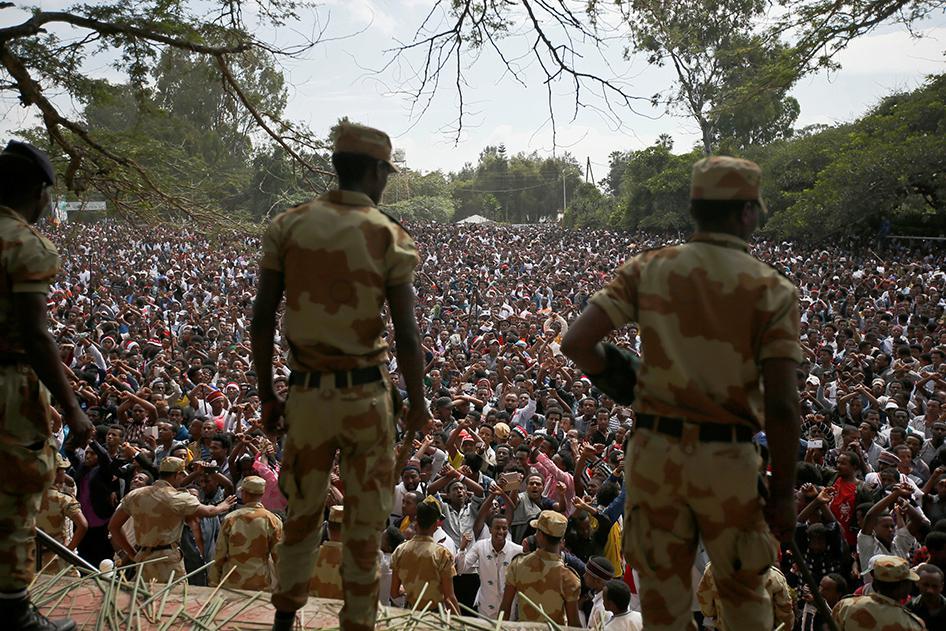 Security officials watch as demonstrators chant slogans while flashing the protest gesture during Irreecha, the thanksgiving festival of the Oromo people, in Bishoftu town, Oromia region, Ethiopia, on October 2, 2016. 