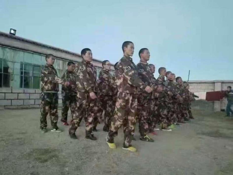一群藏族比丘尼身穿迷彩军服在有围墙的大院中进行军事操练。