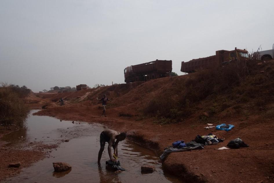 Un homme lave des vêtements en contrebas d’une route minière construite par la Société Minière de Boké (SMB) consortium. Les communautés locales affirment que la construction des routes minières a obstrué et détourné les rivières et les cours d’eau, et en
