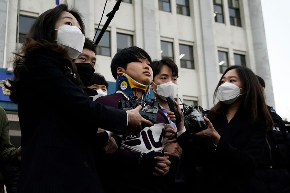 2020년 3월 25일, n번방이라 불리는 온라인 성범죄 조직의 주도자인 조주빈(가운데)이 검찰 조사를 받으러 가기 위해 경찰서를 나서면서 기자들에게 둘러싸여 있다. © 김홍지/Pool Photo via AP