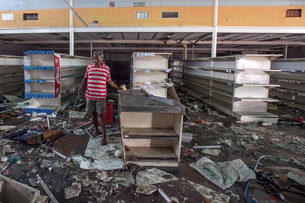 Un hombre busca cualquier resto que pueda recuperar de una tienda de alimentos que fue destruida por cientos de personas durante un saqueo en Cumaná, Venezuela, 16 de junio de 2016. 