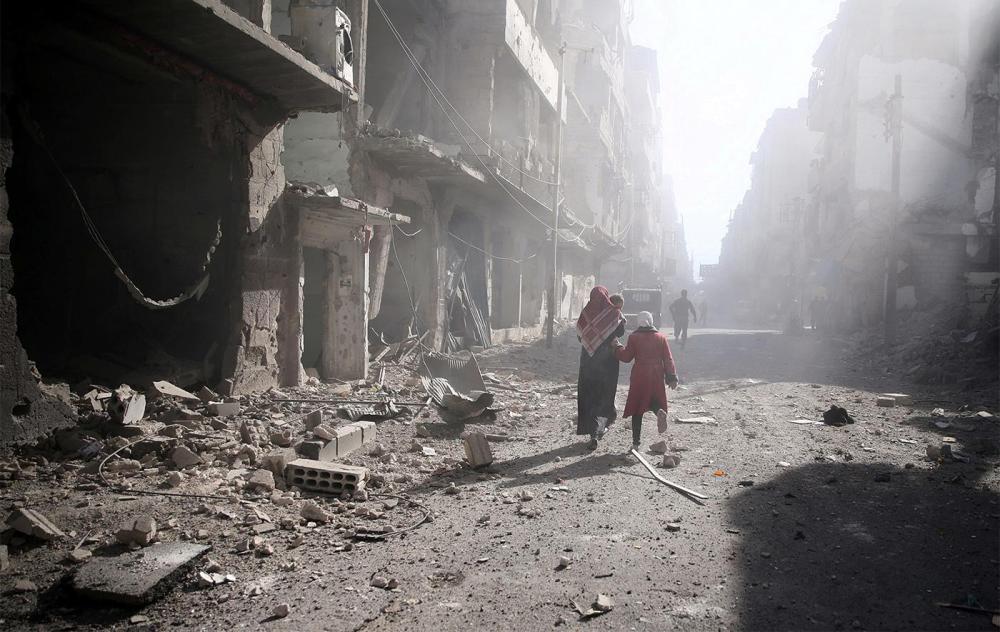 People walk past a damaged site after an airstrike in the besieged rebel-held town of Douma, eastern Ghouta in Damascus, November 2, 2016. 