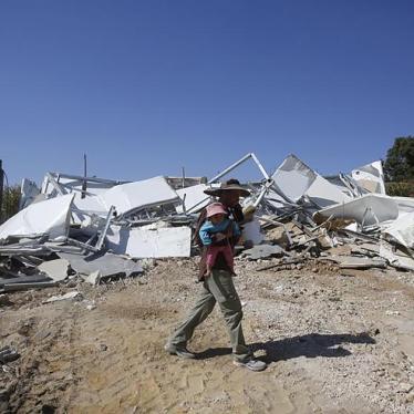 A Palestinian Bedouin carries his child as he walks past his caravan that was demolished by Israeli bulldozers near the Israeli settlement of Karmel, in the village of Um Alkhier near the West Bank city of Hebron October 27, 2014.