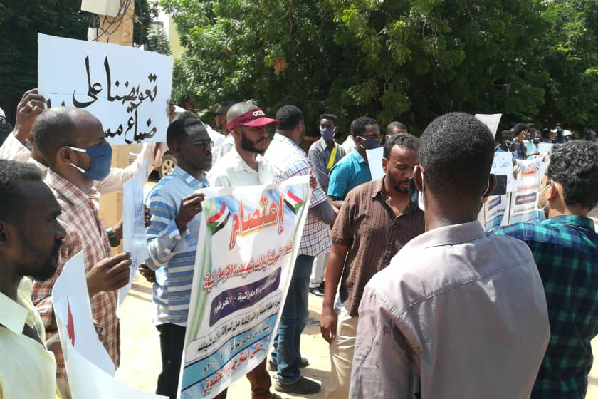 Men in a group hold protest signs written in Arabic