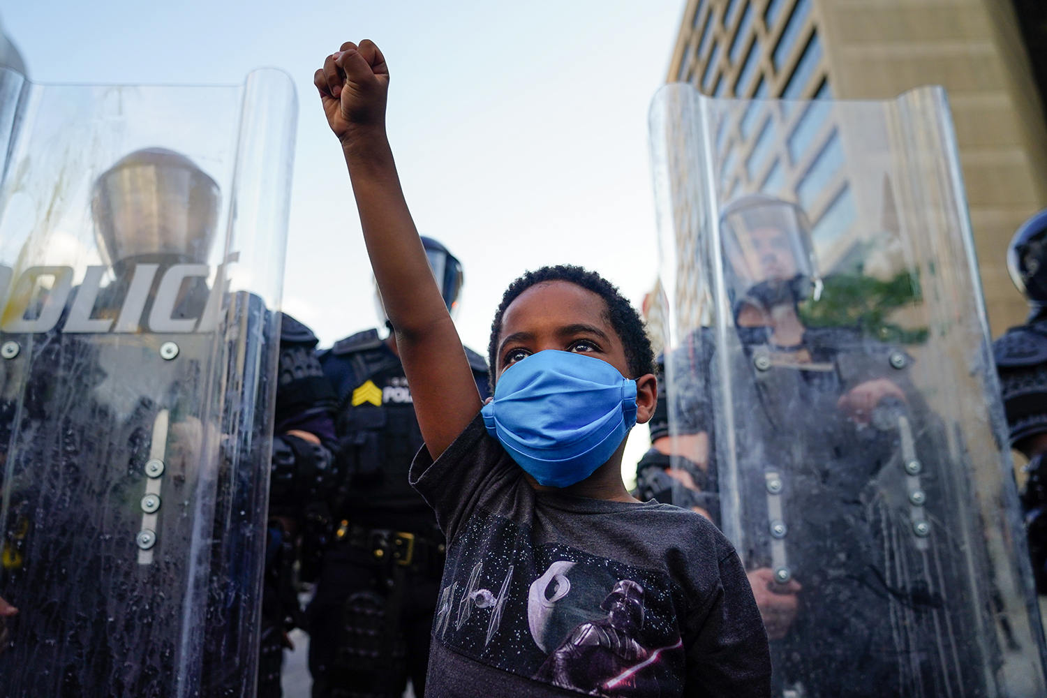 Child raises fist in front of line of police