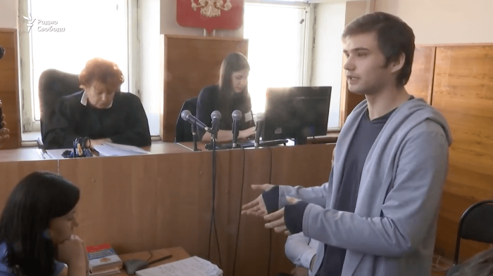 A young man in a hoodie stands in a courtroom speaking to the judges.