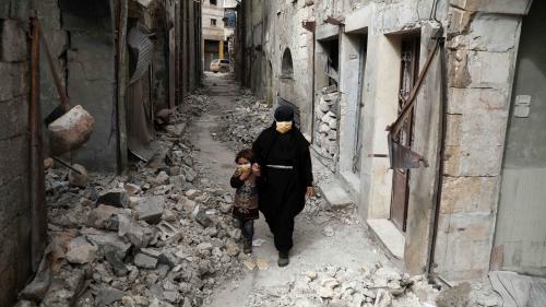 A woman in a black niqab and face mask walks through a deserted street with a child