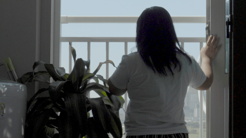 A woman stands by a window.