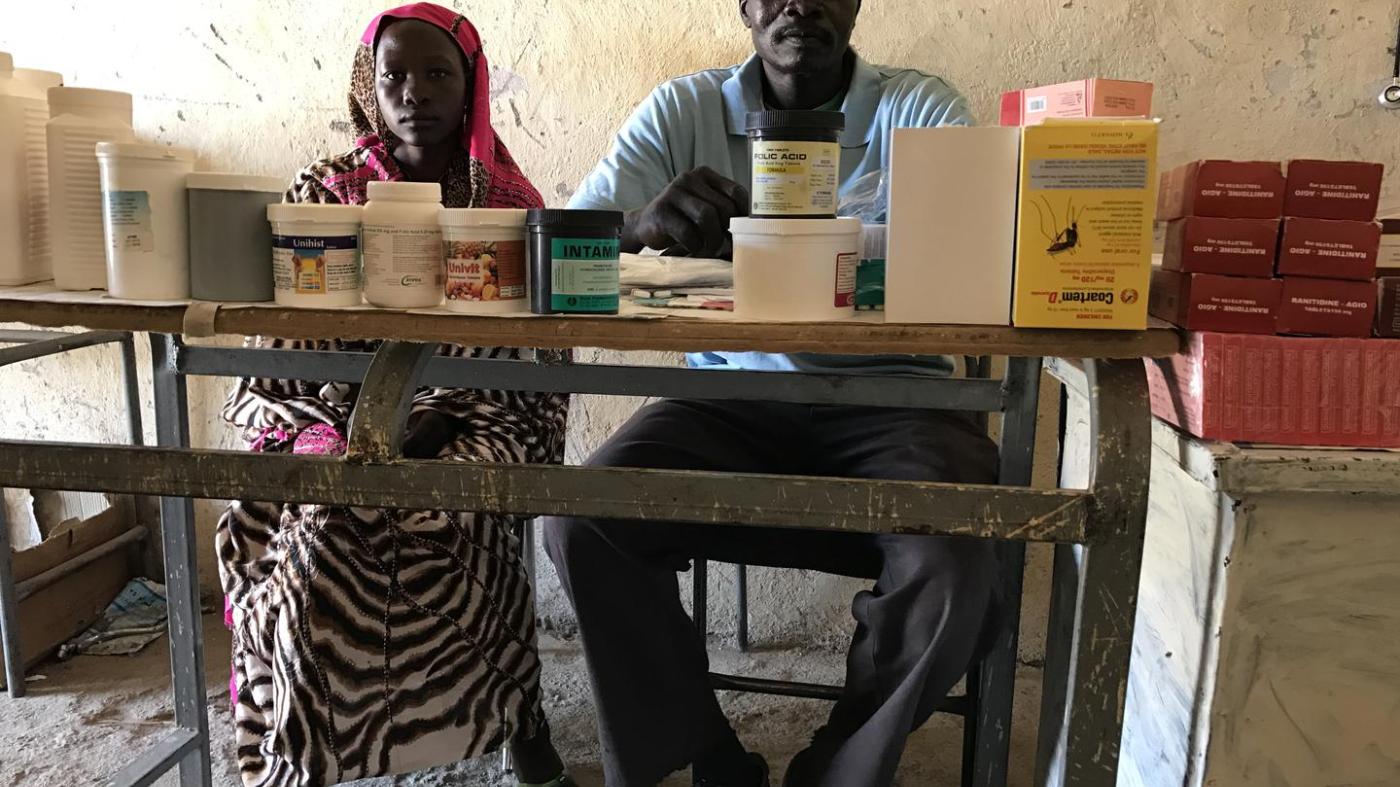 Mukuma Hamad, a volunteer health worker (L), and James Atai, a nurse, sit at a table displaying almost the total stock of basic medicines in the only health clinic in Hadara village, rebel-controlled Southern Kordofan. 