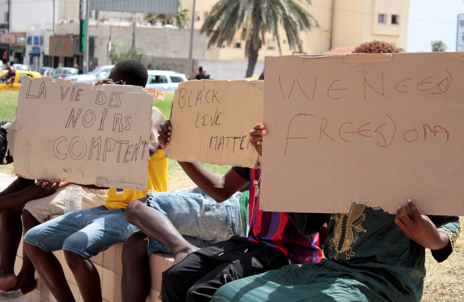 مهاجرون يحملون لافتات كتب عليها بالإنغليزية "حياة السود مهمة" (يسار الصورة بالفرنسية)، خلال تجمع في صفاقس، الساحل الشرقي لتونس، في 7 يوليو/تموز 2023.