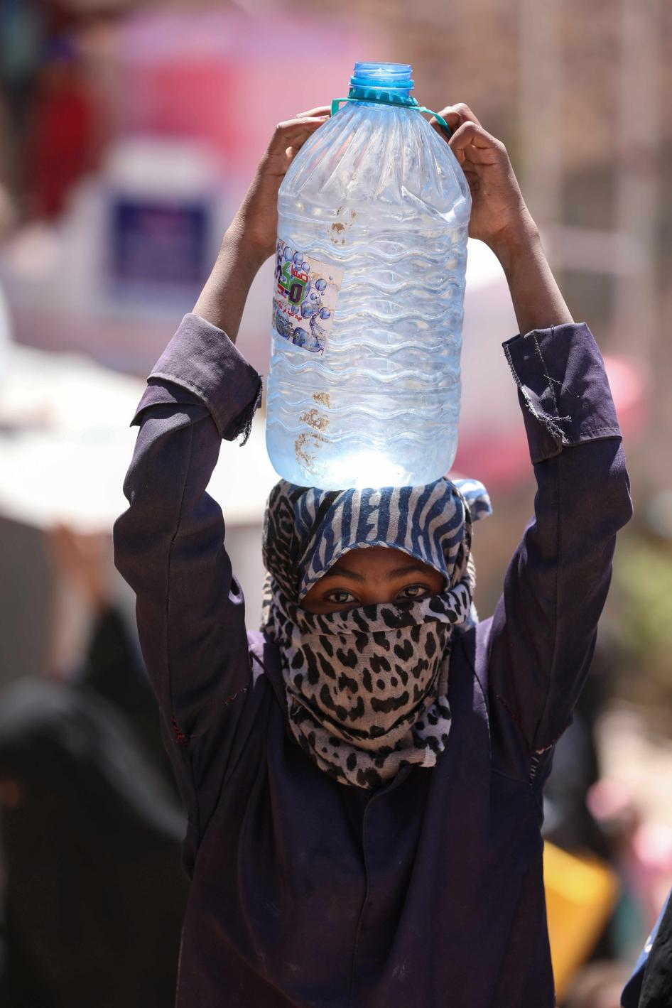 A girl holds a plastic container of water on her head 