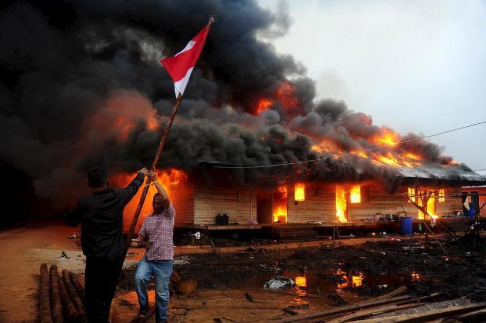 Deux hommes s'emparent d'un drapeau indonésien devant un bâtiment du groupe religieux Gafatar mis à feu par des villageois dans la province du Kalimantan occidental, en Indonésie, le 18 janvier 2016.