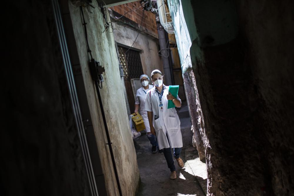Two healthcare workers in masks walk through an alleyway