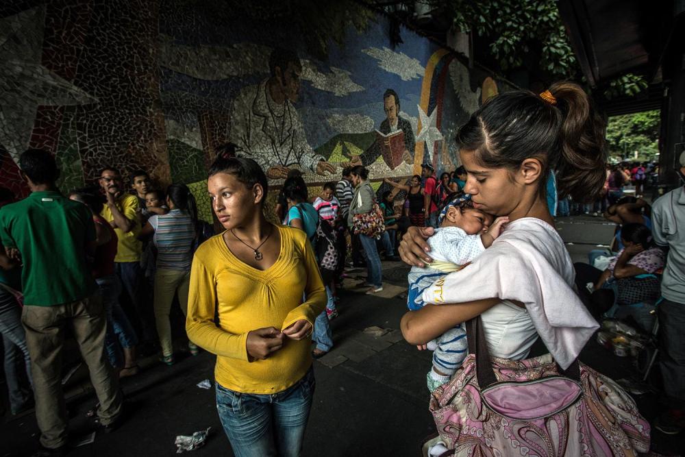 Jailimar Laverde, 17, (left) and Yanny Trejo, 19, (right) wait in a queue of hundreds of people outside a supermarket in Caracas rumored to have received a shipment of corn flour and butter, March 19, 2016.