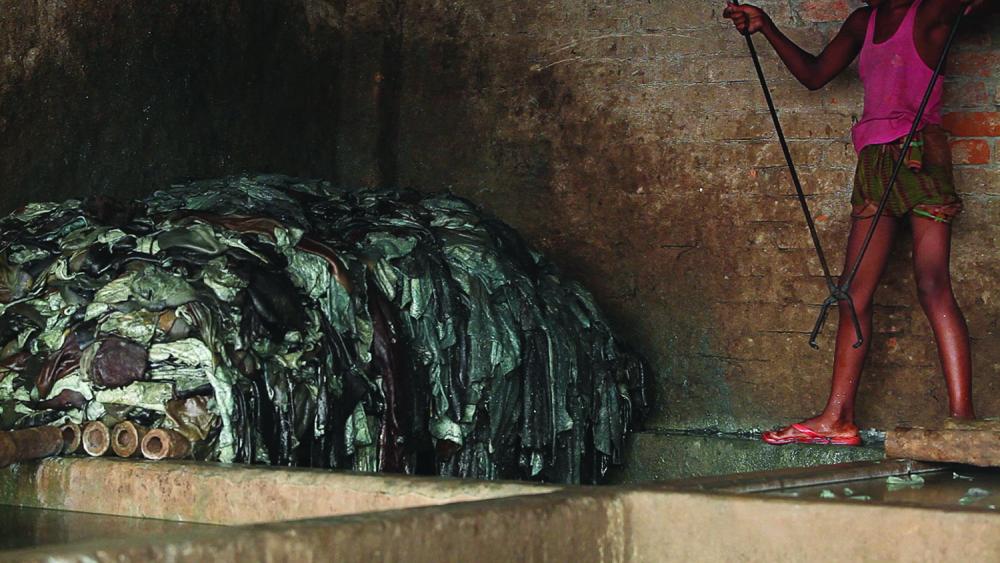 A boy uses tongs to soak hides in a pit of diluted chemicals in a Hazaribagh leather tannery.