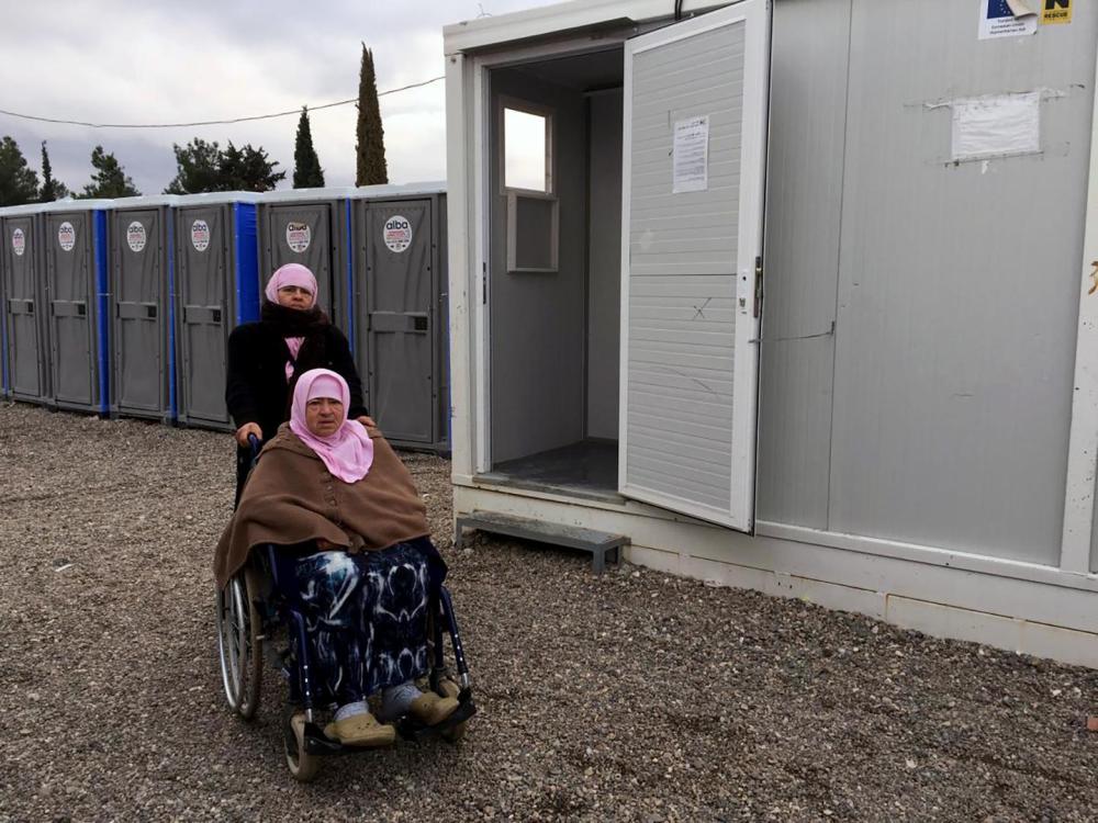 Naima, une femme syrienne handicapée âgée de 70 ans, avec sa fille, Hasne, près d’une douche du camp de réfugiés de Cherso, en Thessalonique, en Grèce. Les douches ne sont pas accessibles pour les personnes circulant en fauteuil roulant. 